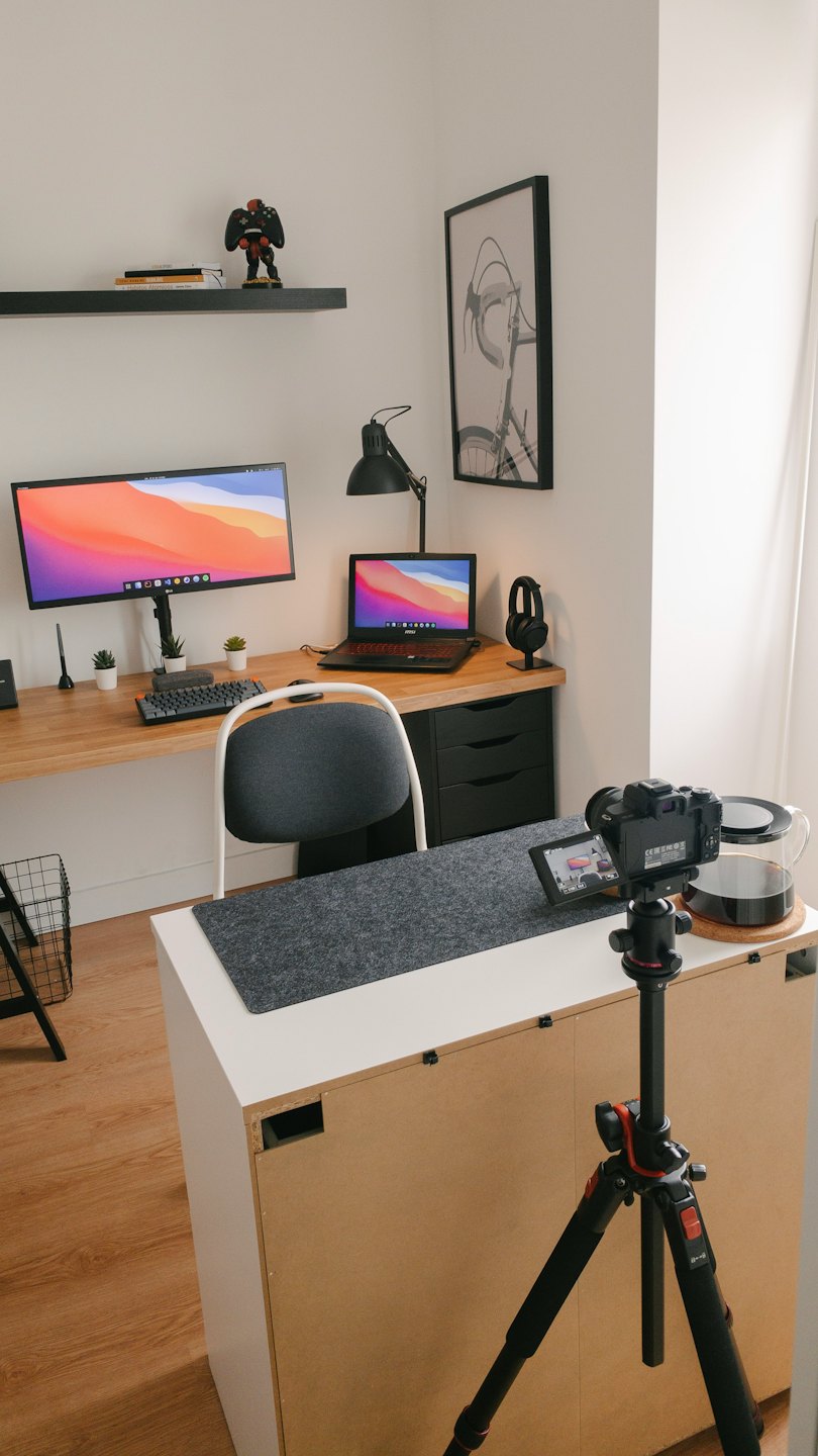 Desk with monitor, laptop, camera, and coffee carafe for content creation.